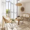A cozy living room scene with rattan furniture, a coffee table, and a large window with sheer curtains. Podgląd zdjęcia produktu