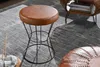 A close-up shot of a brown leather stool with a black metal frame, placed on a gray rug next to a wooden coffee table. Produktbild-Vorschau