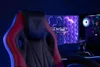 A gaming chair is positioned in front of a computer setup with a monitor displaying a hexagonal pattern and a gaming PC case. Produktbild-Vorschau