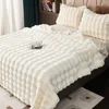 A white plush blanket is neatly spread on a bed, with two matching pillows at the headboard. A teacup and saucer are placed on the blanket. Produktbild-Vorschau