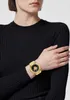 A person wearing a black sweater and a gold watch on their left wrist. Podgląd zdjęcia produktu