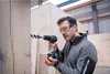 A man is using a cordless drill to drill a hole in a wooden board in a workshop. Náhled obrázku produktu