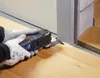 A person wearing gloves uses an oscillating multi-tool to cut along the base of a door frame. Podgląd zdjęcia produktu