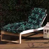 A chaise lounge with a tropical leaf patterned cushion is placed on a wooden deck, with lush green foliage in the background. Náhled obrázku produktu