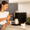 A woman is using a coffee machine in a kitchen setting. Produktbild-Vorschau