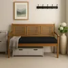 A wooden bench with a black cushion, placed in a room with a painting on the wall and a vase with flowers. Produktbild-Vorschau