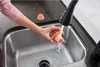 A person is rinsing a small orange filter under a kitchen faucet. Produktbild-Vorschau