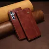 A brown leather phone case is shown on a brown background with rolled leather pieces. Produktbild-Vorschau