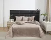 A neatly made bed with a beige quilted bedspread and pillows, set against a black upholstered headboard. Podgląd zdjęcia produktu