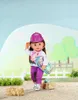 A doll dressed in riding attire, standing in an outdoor setting with hay bales and a fence. Produktbild-Vorschau
