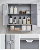 A wall-mounted bathroom cabinet with its doors open, displaying its contents and details of its hardware. The cabinet is gray and has two shelves. It contains various bathroom products like bottles, jars, and toilet paper rolls. Two smaller images show the Náhled obrázku produktu
