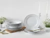 A set of white porcelain plates and bowls are arranged on a white surface, with two white candles in the background. Náhľad obrázku produktu