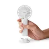 A hand holding a white portable fan with a white base. Produktbild-Vorschau
