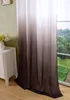 A close-up view of a curtain with a gradient color effect, hanging next to a window with a view of trees. Produktbild-Vorschau