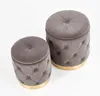 Two gray upholstered ottomans with gold bases are shown against a white background. Produktbild-Vorschau
