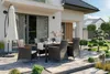 An outdoor patio set with a table and chairs, set up on a paved patio next to a modern house. Náhľad obrázku produktu