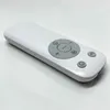 A white remote control is displayed on a white and light gray surface. Produktbild-Vorschau