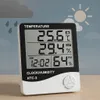 A digital thermometer and hygrometer is displayed on a wooden surface against a background depicting weather icons. Anteprima dell’immagine prodotto