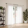A room with white curtains, a black shelf with plants and decor, and a large potted plant. Podgląd zdjęcia produktu