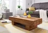 A living room scene with a wooden coffee table in the foreground, a sofa and a window in the background. Náhled obrázku produktu