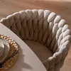 A close-up view of a beige upholstered dining chair with a textured weave, next to a table with a placemat and plate. Produktbild-Vorschau