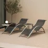 Two lounge chairs and a small table are set up on a textured outdoor surface, with a small tree and a wall in the background. Voir les images du produit