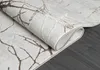 A close-up view of a rolled-up rug with a branch-like pattern, lying on a dark wooden floor. Náhled obrázku produktu