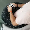 A person playing a video game while sitting on a large, round pillow with a pattern of game controller symbols. Anteprima dell’immagine prodotto