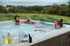 A couple relaxing in a hot tub outdoors with a scenic background. Produktbild-Vorschau