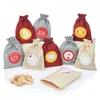 A collection of small, drawstring fabric bags, some red and some gray, arranged on a white surface. Several bags have circular labels with numbers and festive designs. A pile of small wooden clothespins is in the foreground, and one beige bag is open. Produktbild-Vorschau