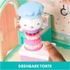 A child's finger is pressing a button on a toy kitchen set, which features a cake-shaped tower with a cat character on top. Produktbild-Vorschau