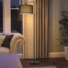A floor lamp illuminates a living room corner with a sofa and curtains. Produktbild-Vorschau