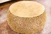 A round coffee table with a gold, intricate metal base and a textured gold top, placed on a patterned rug. Produktbild-Vorschau