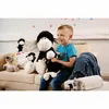 A young boy is sitting on a couch with several stuffed animals, including a large black sheep. Produktbild-Vorschau