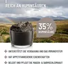 A product shot of a dark, mud-like substance in a glass container, set against a landscape background with mountains and a rainbow. Produktbild-Vorschau