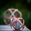 Two spherical metal lanterns with candles inside, placed on a wooden surface with a blurred green background. Voir les images du produit