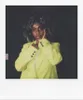 A woman in a bright yellow blazer poses with her hands on her face against a dark background. Náhled obrázku produktu