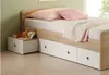 A child's bed with storage drawers, a bedside table with a toy and books, and pillows and a blanket on the bed. Produktbild-Vorschau