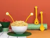A playful arrangement of pasta and serving utensils with googly eyes, set against an orange background. Podgląd zdjęcia produktu