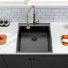 A black kitchen sink with a silver faucet is shown on a white countertop with a tiled backsplash. Náhled obrázku produktu