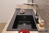 A black kitchen sink with a chrome faucet is shown on a wooden countertop. There are some red currants in the foreground and a dish brush and soap on the right side. Produktbild-Vorschau