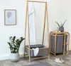 A minimalist interior scene featuring a bamboo clothes rack with a white towel and a storage basket, a potted plant, and a small side table with a plant and toiletries. Anteprima dell’immagine prodotto