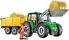 A green tractor with a yellow trailer and hay bales, with a farmer figure standing next to it. Voir les images du produit