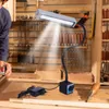 A person is working at a workbench with a magnetic LED work light illuminating the area. Tools and shelves are visible in the background. Podgląd zdjęcia produktu