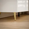 A close-up view of the bottom part of a white cabinet with gold legs. Produktbild-Vorschau