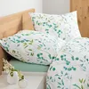 A close-up view of bedding with a floral pattern, including pillows and a duvet cover, set against a wooden headboard and a nightstand with vases. Produktbild-Vorschau