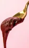 A close-up shot of a spoon holding a dollop of dark brown spread, with a pink background. Produktbild-Vorschau