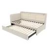 A beige upholstered daybed with a pull-out trundle bed is shown against a white background. The daybed has a tufted headboard and a built-in shelf unit at the back. The wooden slats of both the main bed and the trundle are visible. Náhled obrázku produktu