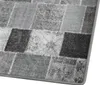 A close-up view of a patchwork rug with various shades of gray and black squares. Produktbild-Vorschau