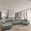 A modern living room with a large sectional sofa in the foreground and a fireplace and windows in the background.